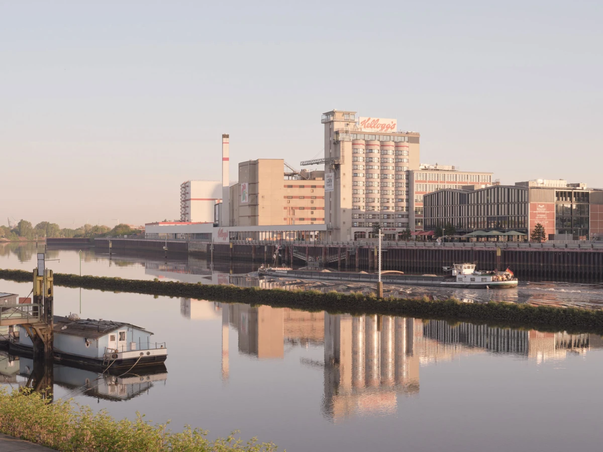 Kellogg's cereal factory on the riverfront, with a small barge passing; reflections shimmer in the calm water.