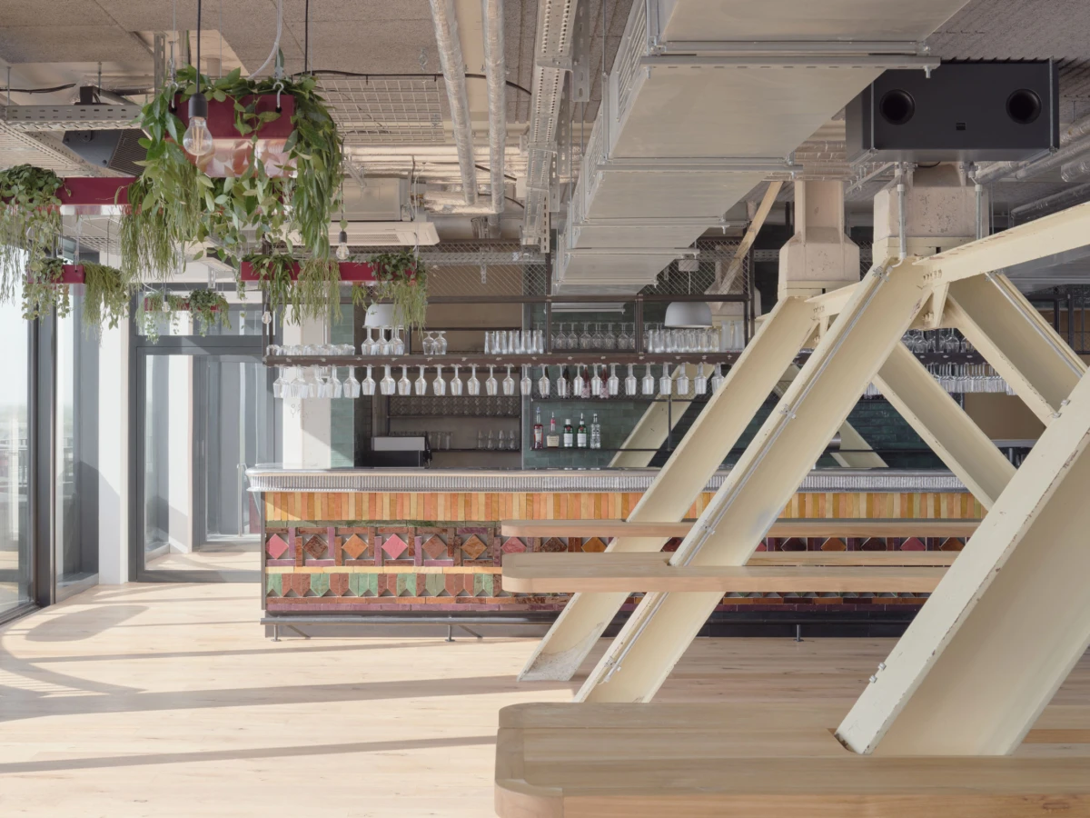 Modern cafe bar interior with suspended plants and glassware above a tiled counter.