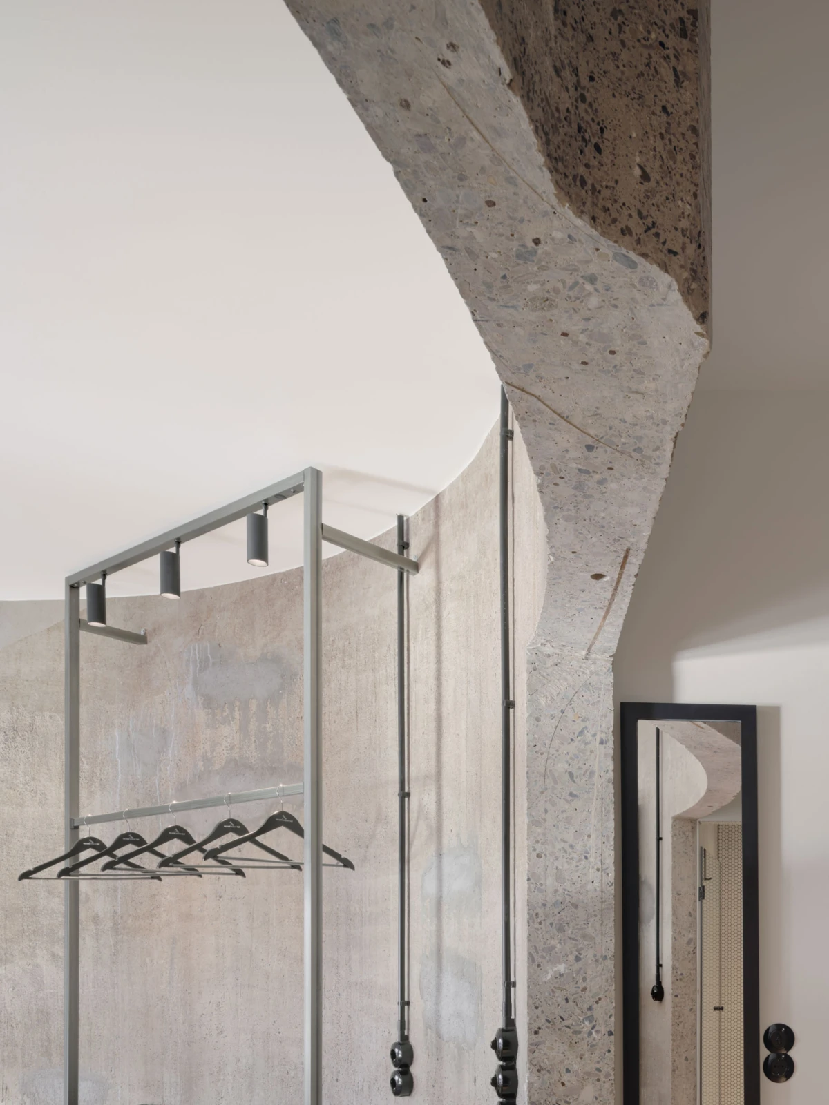 Metal clothing rack with black hangers in a modern industrial interior featuring a curved concrete wall.
