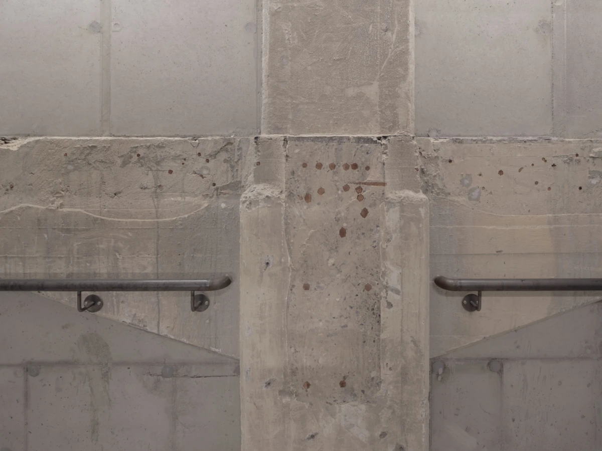 Central concrete pillar with metal handrails on both sides attached to a stained wall with rust spots.