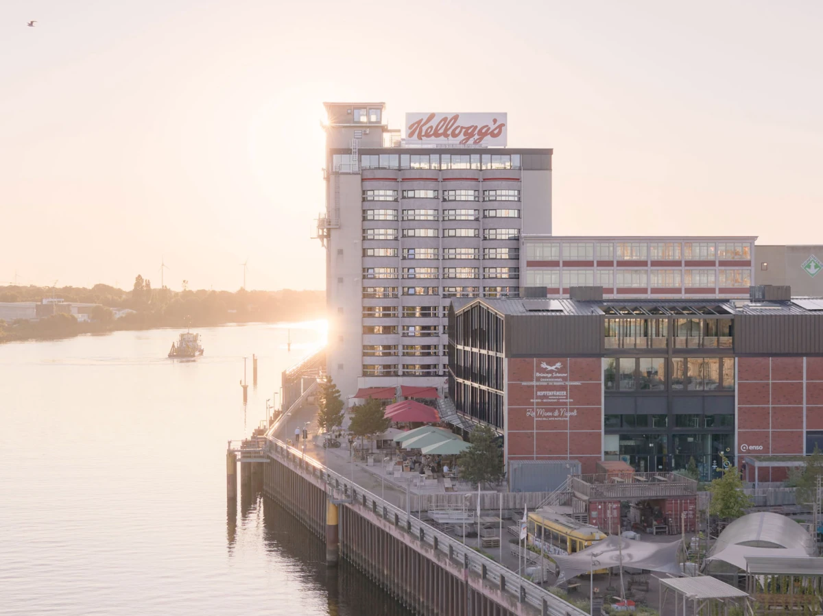 Riverfront office and retail complex with Kellogg's sign; promenade with outdoor seating along the water at sunset.