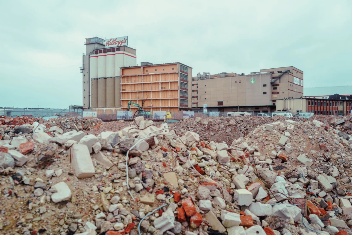 Rubble-filled construction site with an excavator, Kellogg's cereal plant and industrial buildings in the background.