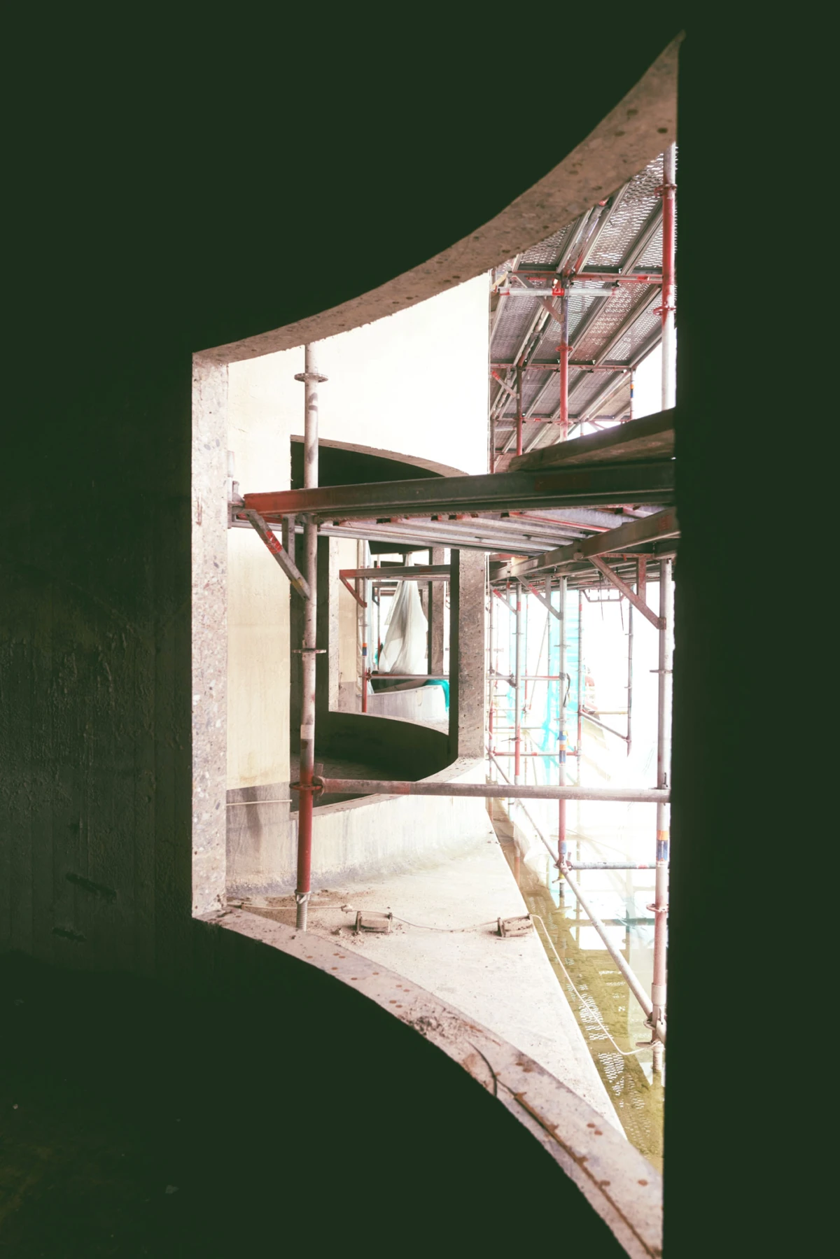 Red metal scaffolding inside a curved concrete opening at a construction site.