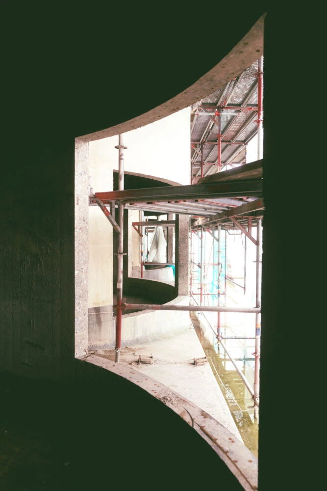 Interior construction site featuring red scaffolding along a curved concrete wall opening.