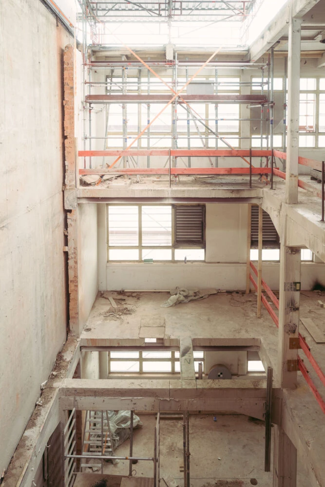 Interior of a multi-story building under construction, with crisscrossing metal scaffolding and orange safety rails.