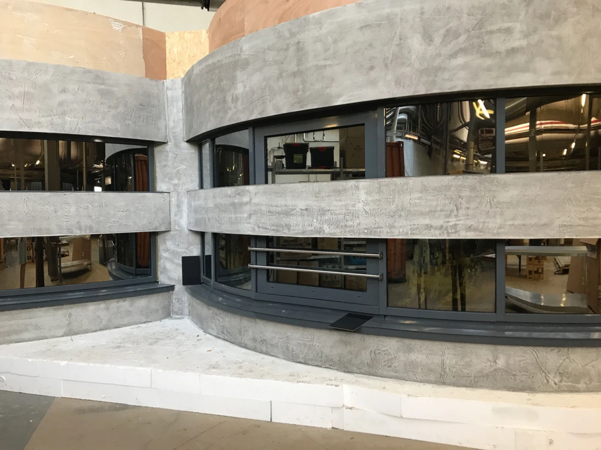 Curved concrete wall with large dark-gray framed windows and metal railing in a modern interior under construction