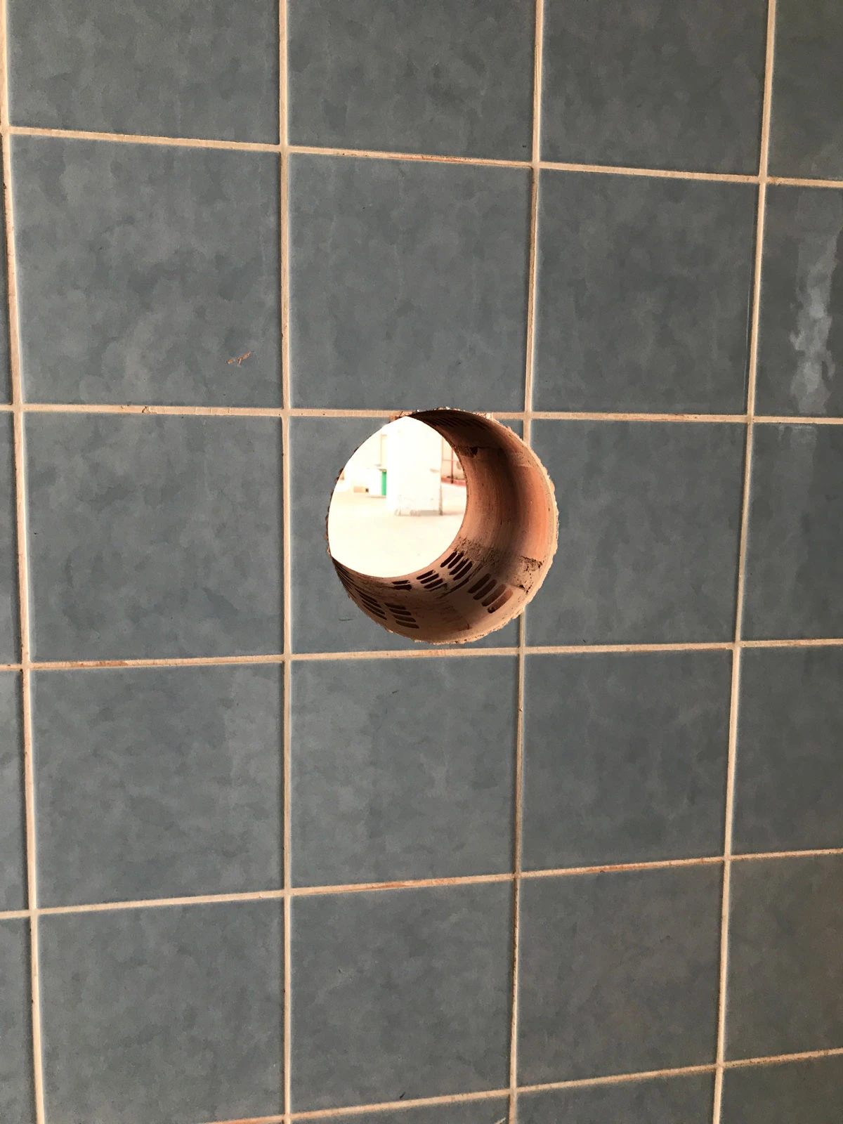 Blue tiled wall with a circular hole, revealing a brown cardboard tube through the opening.
