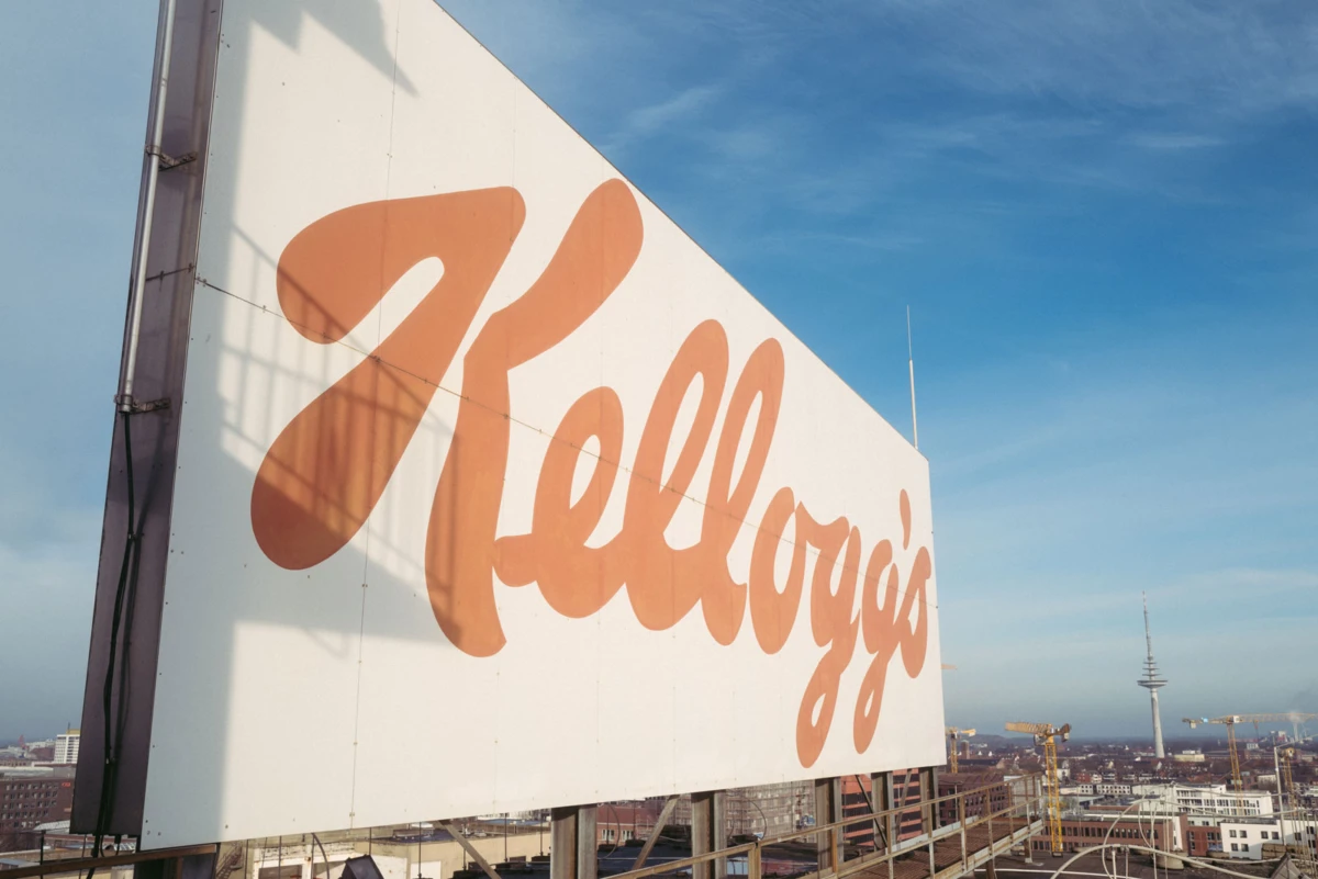 Kellogg's billboard on a rooftop overlooking a city skyline under a blue sky.