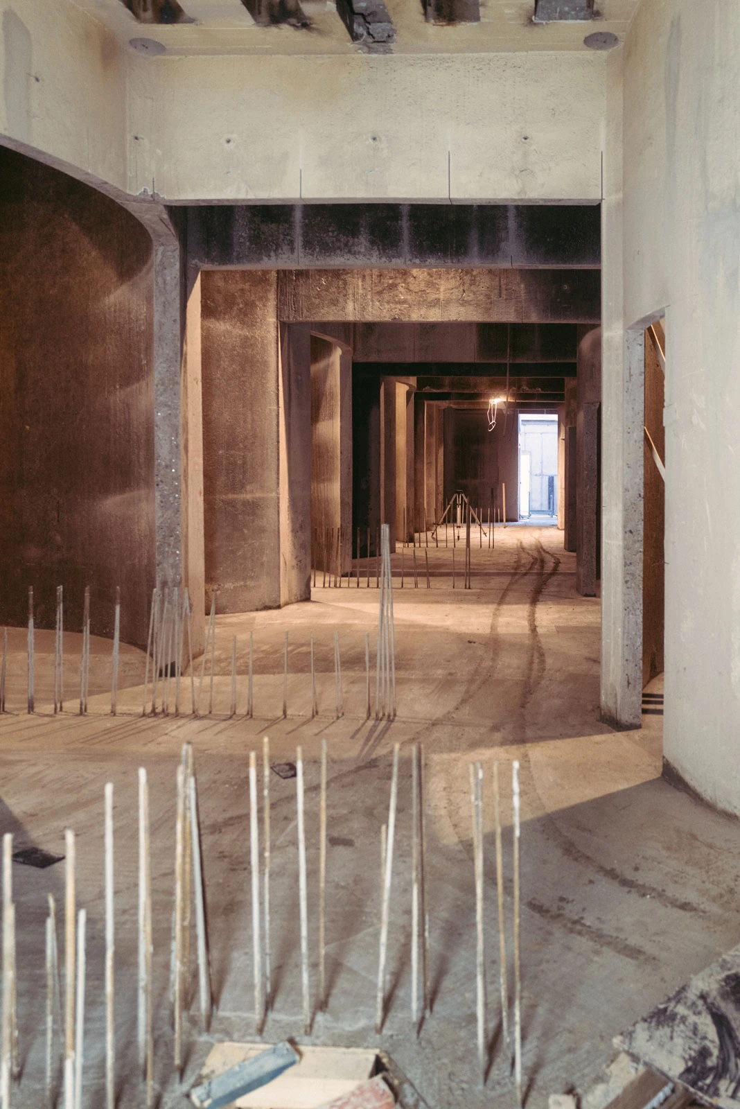 Unfinished concrete hallway under construction with vertical steel rebar protruding from the floor.