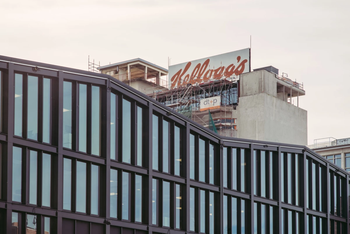 Glass-fronted office building in foreground; construction site with Kellogg's sign in background.