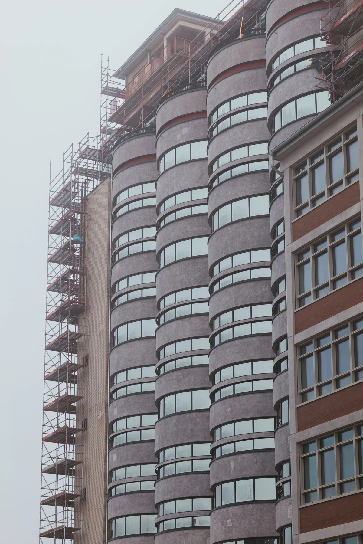 Modern high-rise with cylindrical glass tower sections; extensive scaffolding along the left side during construction.