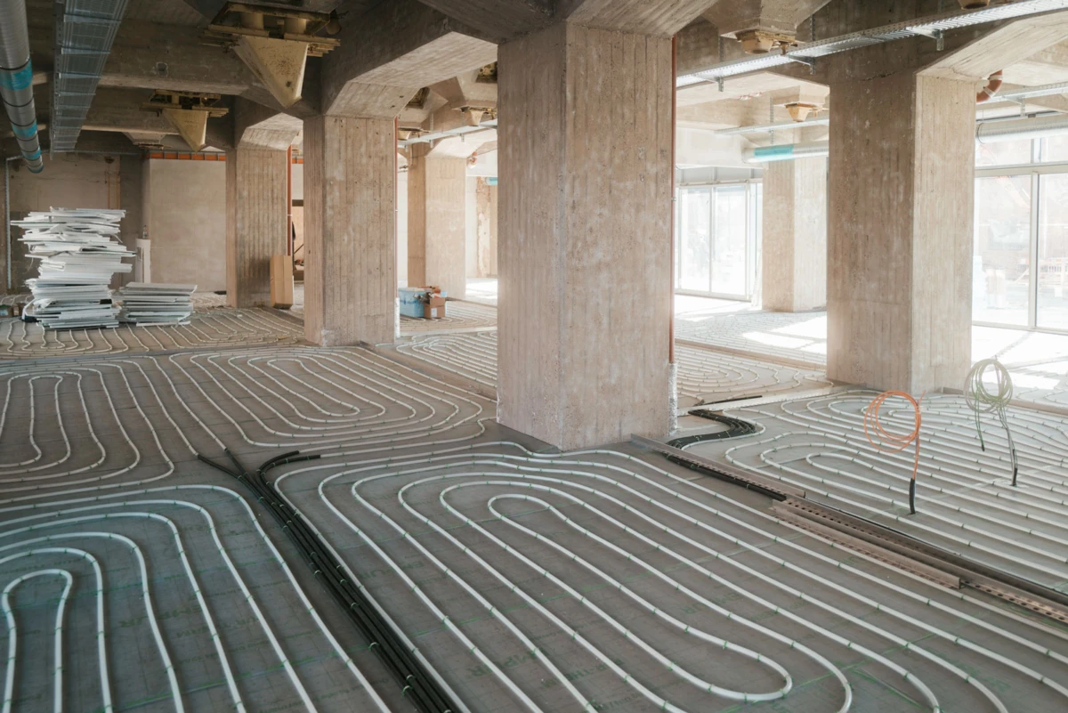 Unfinished building interior with radiant floor heating tubes laid out on the concrete floor; concrete columns and large windows.