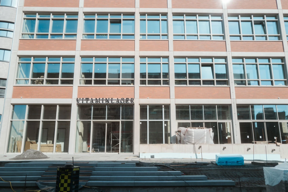Under-construction brick-and-glass storefront with 'VITAMINLAGER' sign; construction debris and equipment on the front steps.