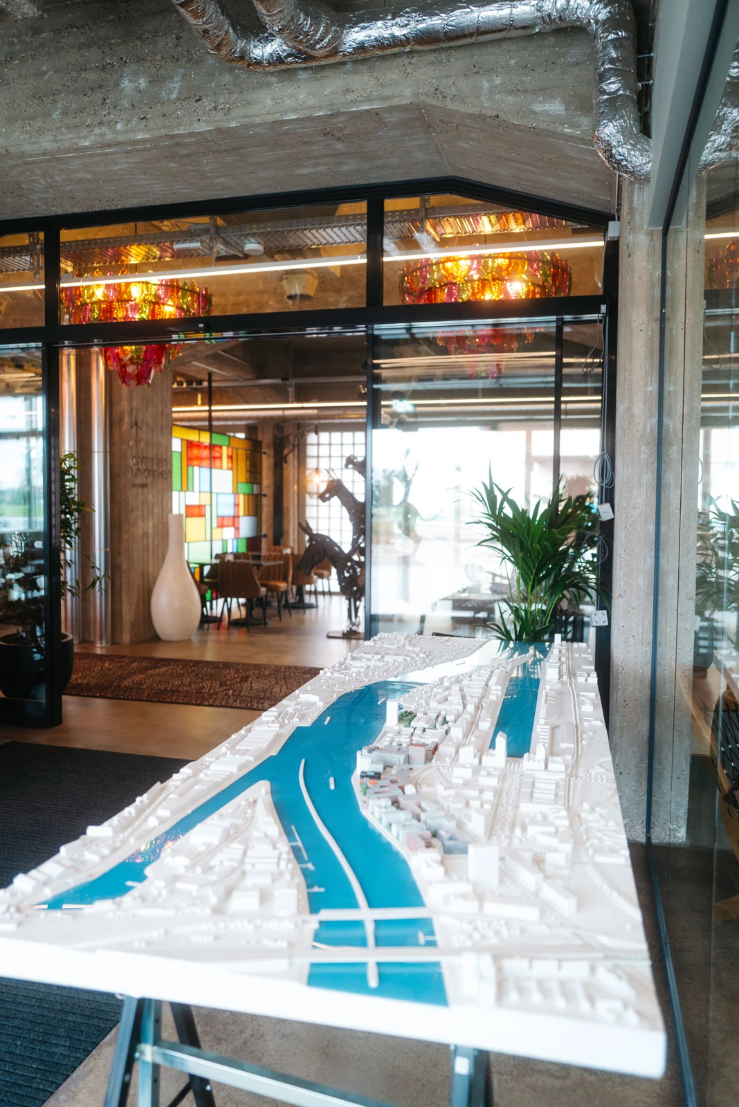 White scale-model city with a blue river on a display table in a modern glass-walled office lobby.