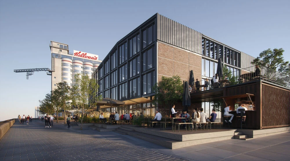 Outdoor cafe on a two-level terrace beside a modern glass-brick building; people sit at tables while a Kellogg’s sign dominates the background.