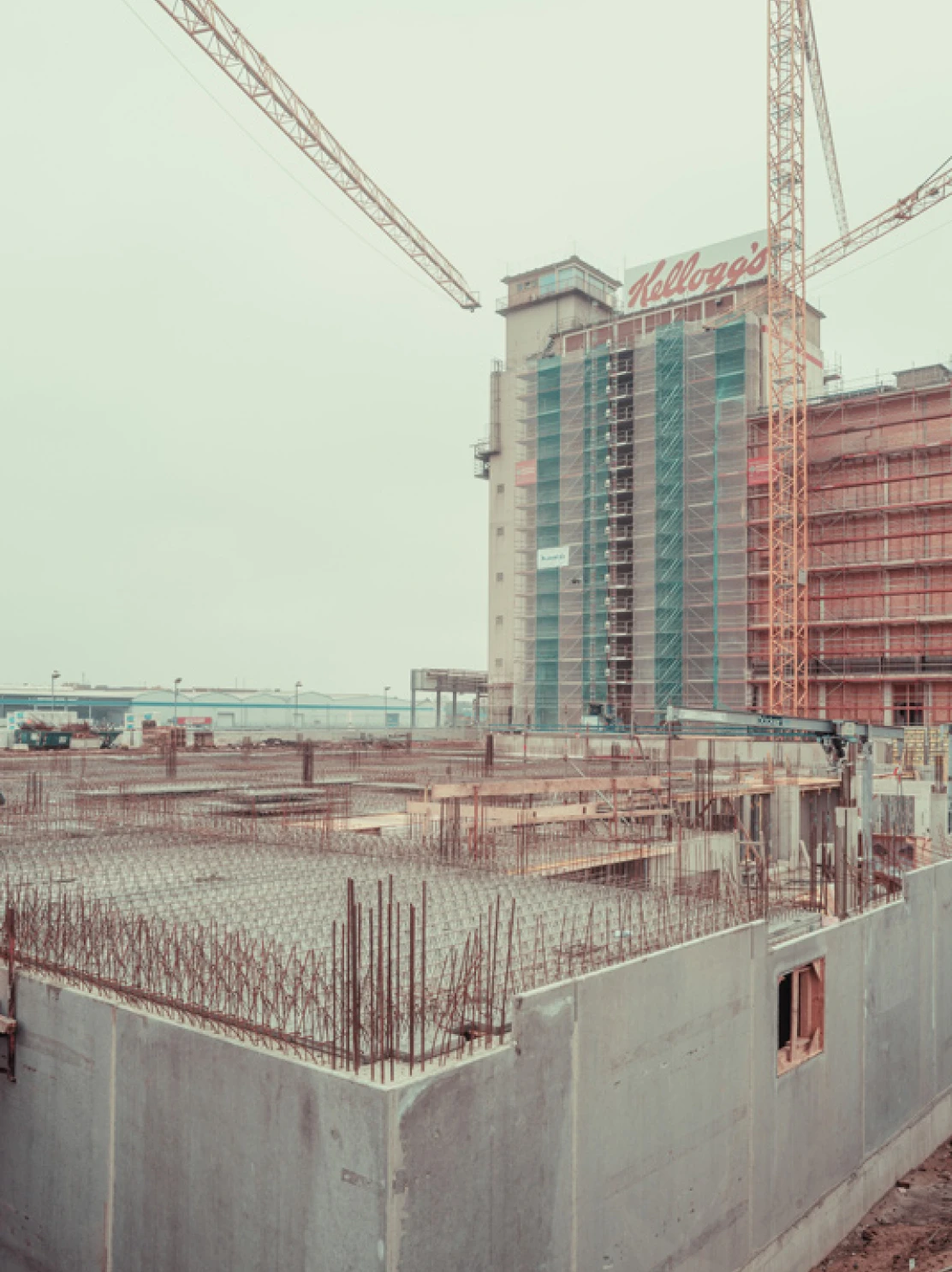 Construction site with tall building under construction bearing Kellogg's sign, cranes overhead, concrete barriers and rebar.