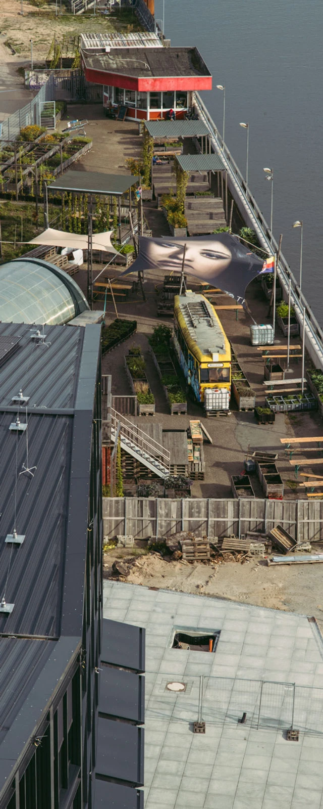 Yellow tram parked on a riverside promenade with a large close-up banner of a face and a red-roofed kiosk nearby.