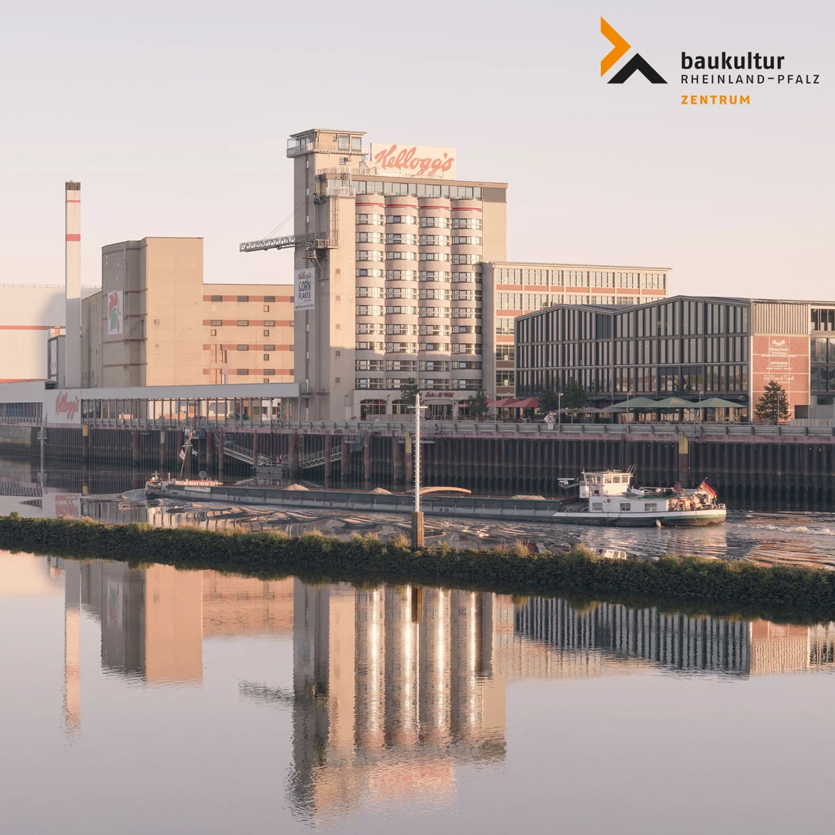 Kellogg's sign atop a tall industrial building beside a riverfront; boats on calm water with reflections.