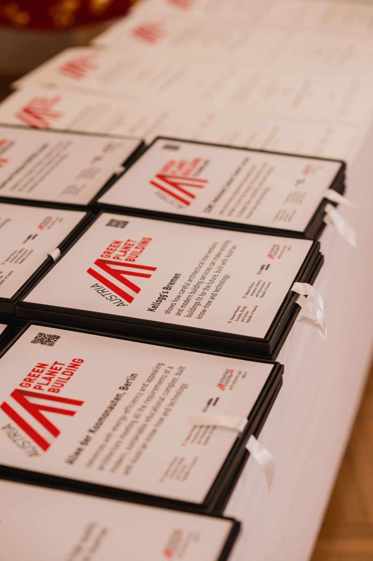 Several framed certificates on a table display a red diagonal logo and the text Green Planet Building.