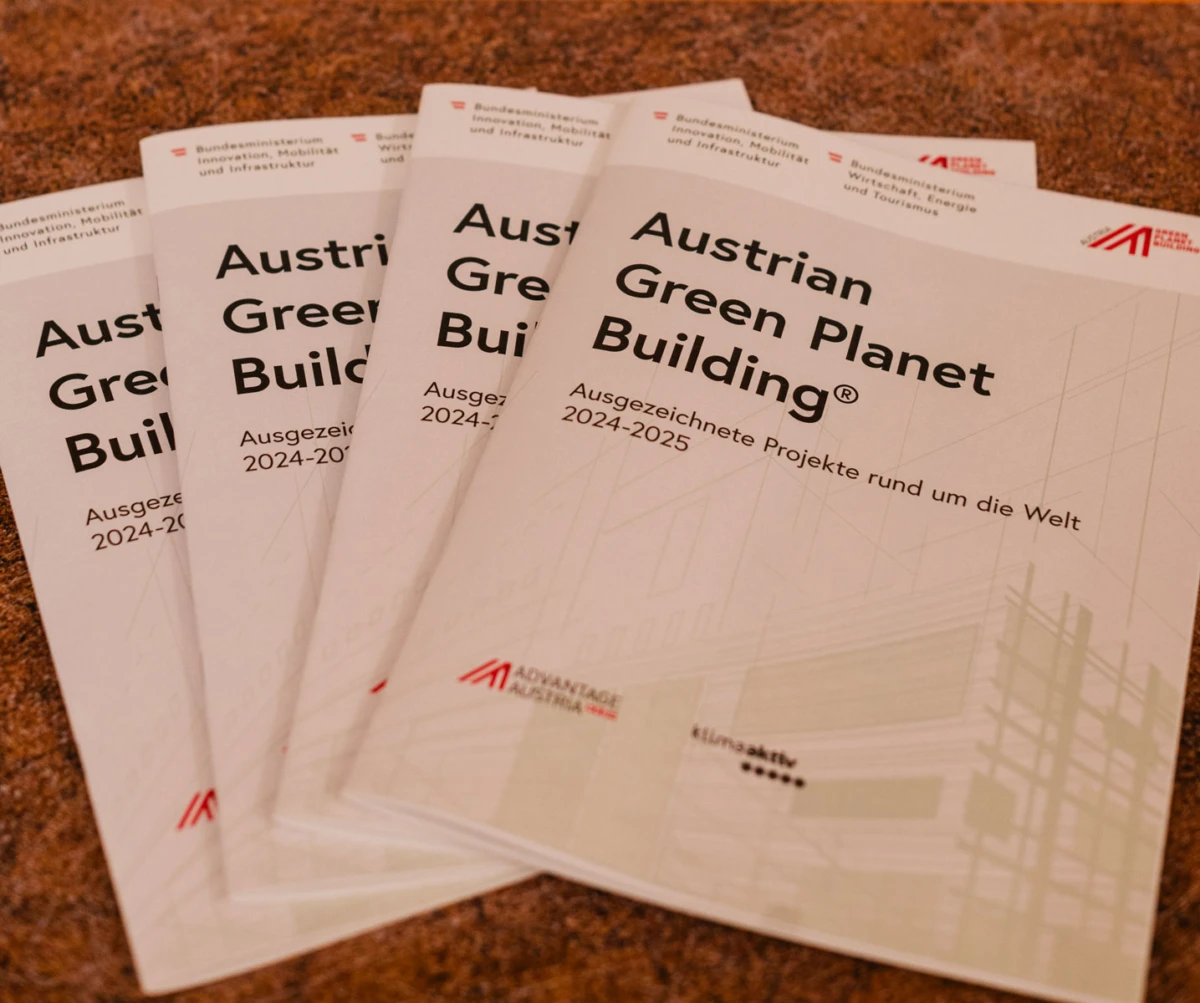 Three Austrian Green Planet Building brochures fanned on a brown carpet.