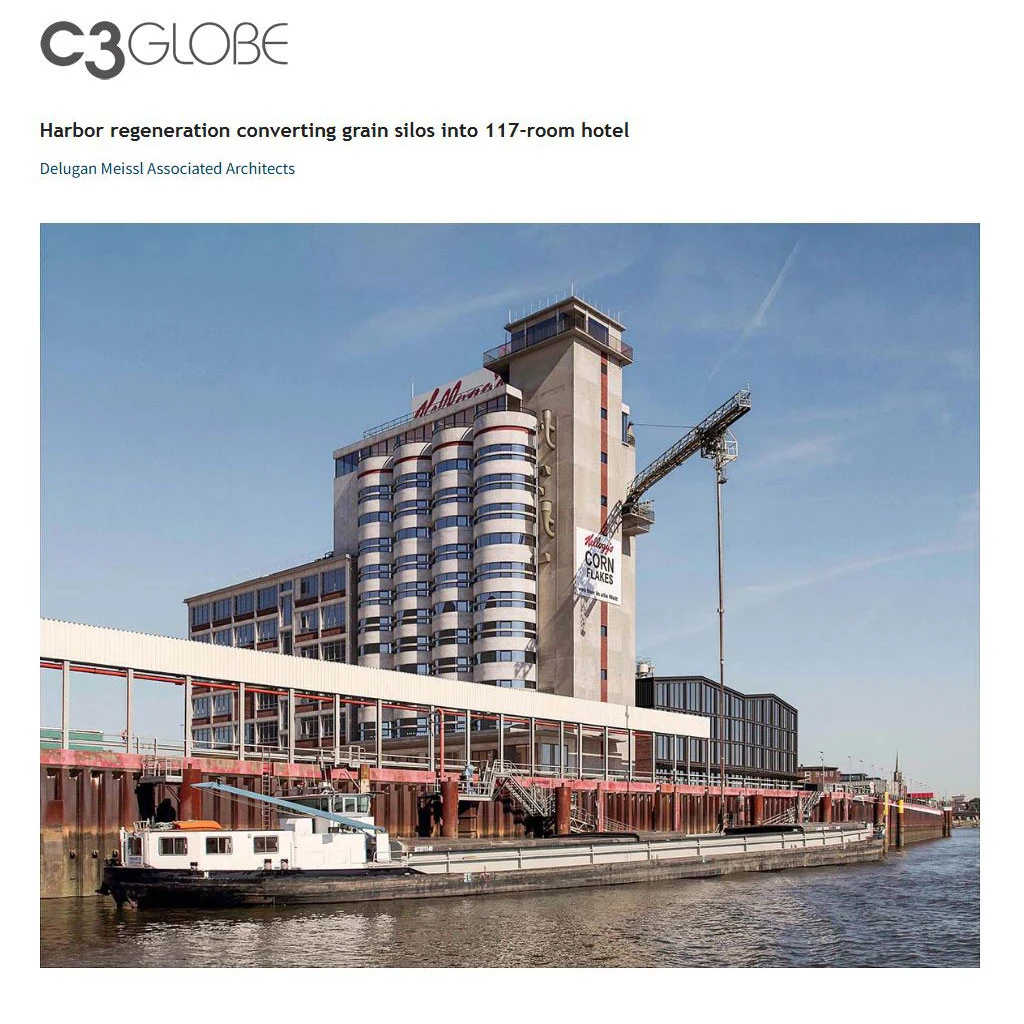 Harbor construction site with cylindrical grain silos attached to a riverfront hotel-like building and a crane.