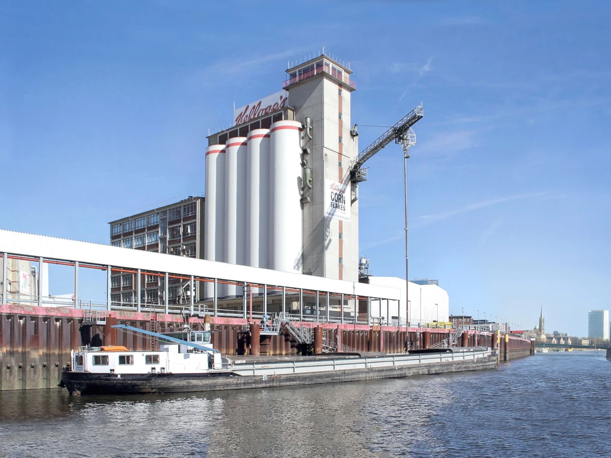 Kellogg's cereal plant with tall silo towers along a riverfront; a barge is docked at the quay.
