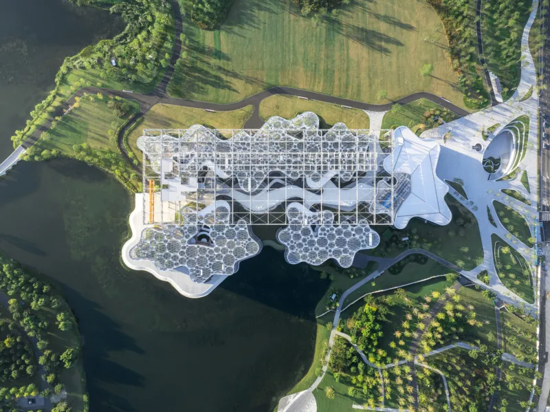 Aerial view of a futuristic glass-domed complex with bubble-like modules over a lake, linked by white curving walkways through a green park.
