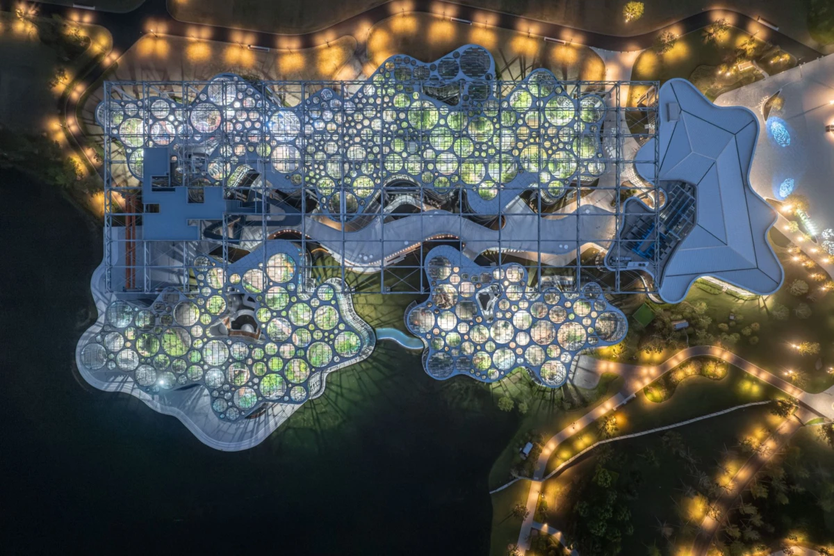 Aerial view of a futuristic complex of interconnected glass domes and winding walkways over a water body, lit at night.