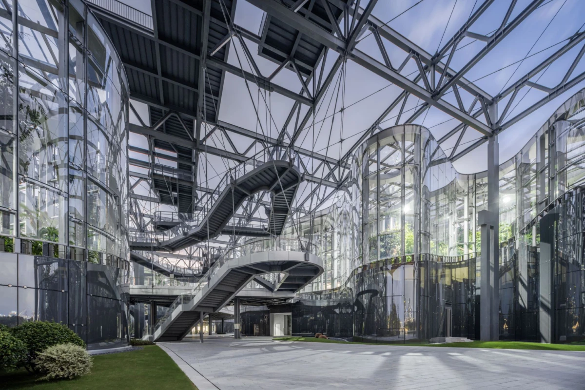 Empty glass atrium with curved escalators and exposed steel framework.