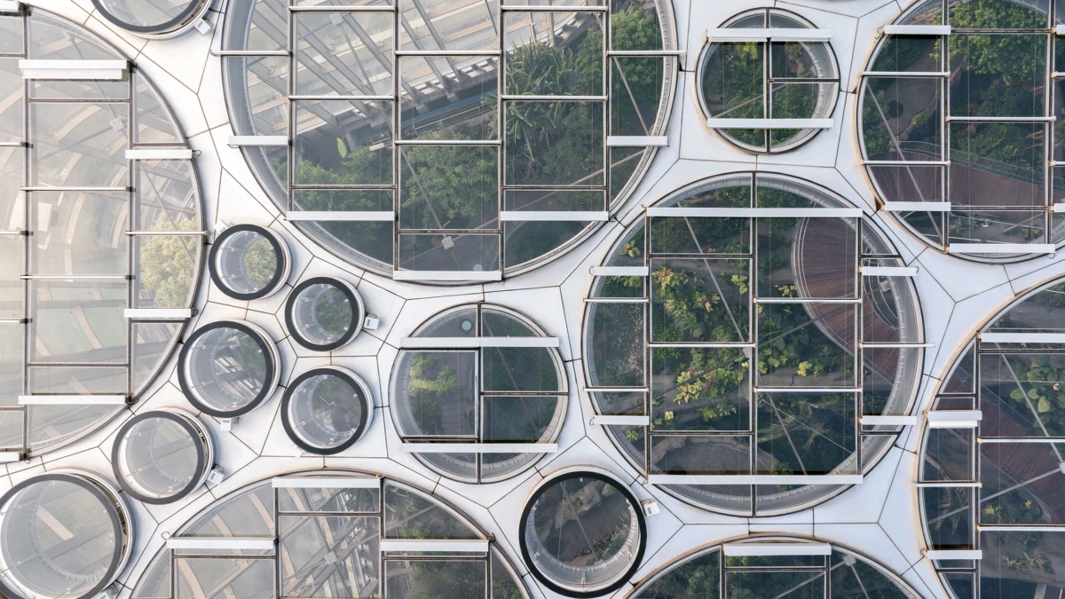 Aerial view of a modern building facade with circular glass windows and metal grids, showing greenery inside.