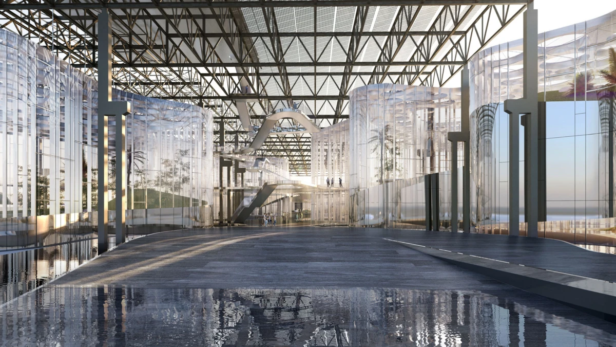 Interior of a glass atrium with a steel lattice roof, a central curved pedestrian bridge, and a reflective floor.