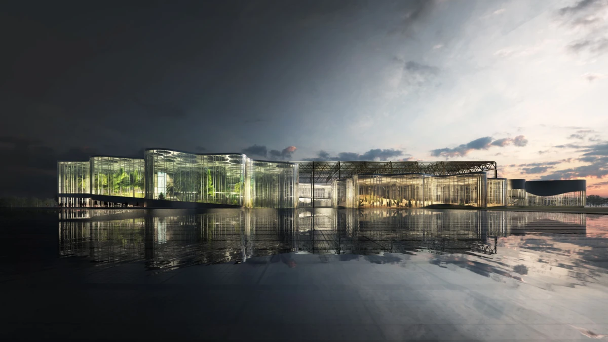Glass-walled building complex on a calm waterfront at dusk, illuminated interiors with greenery, reflected in the water.