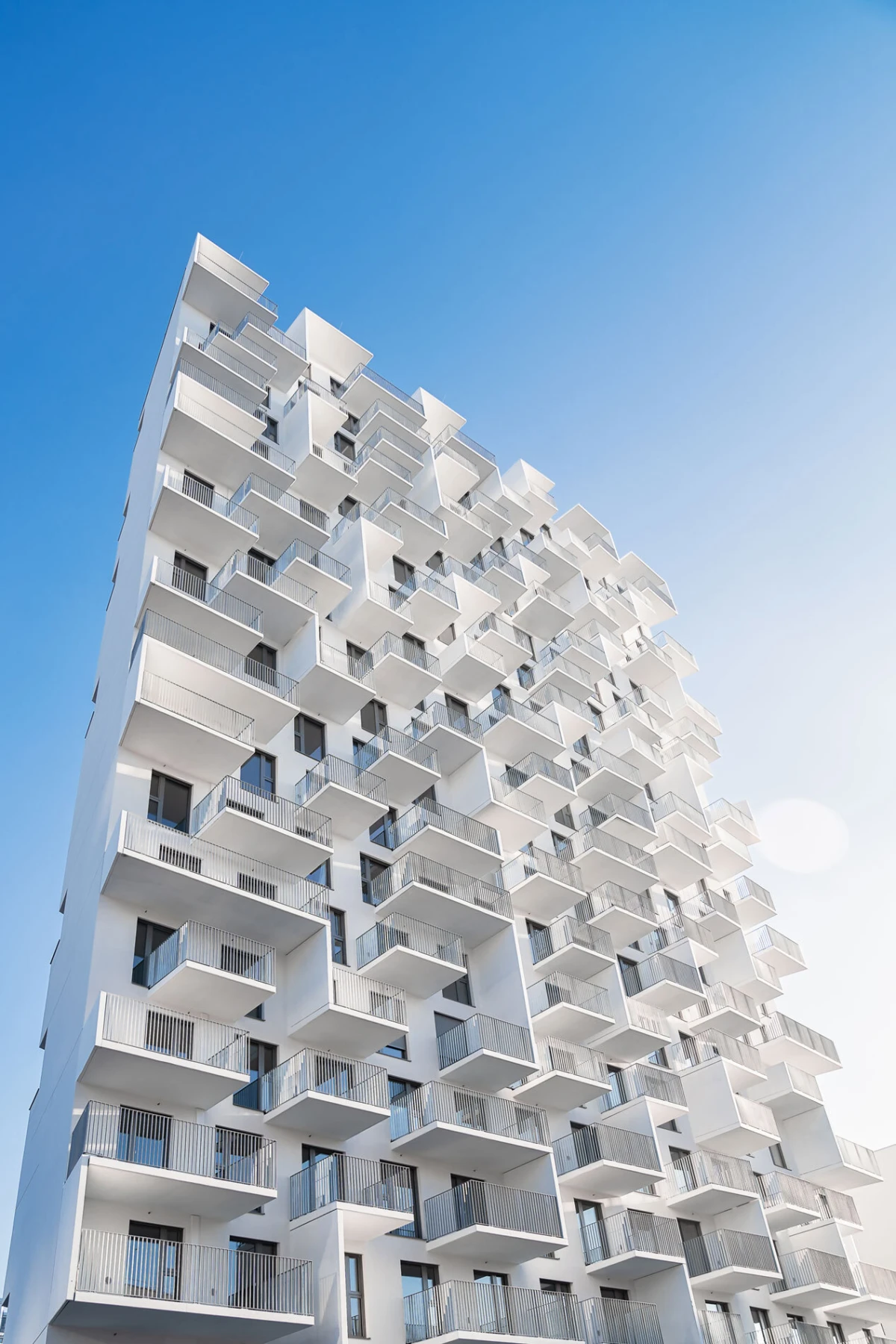 White high-rise apartment building with numerous protruding balconies against a clear blue sky.