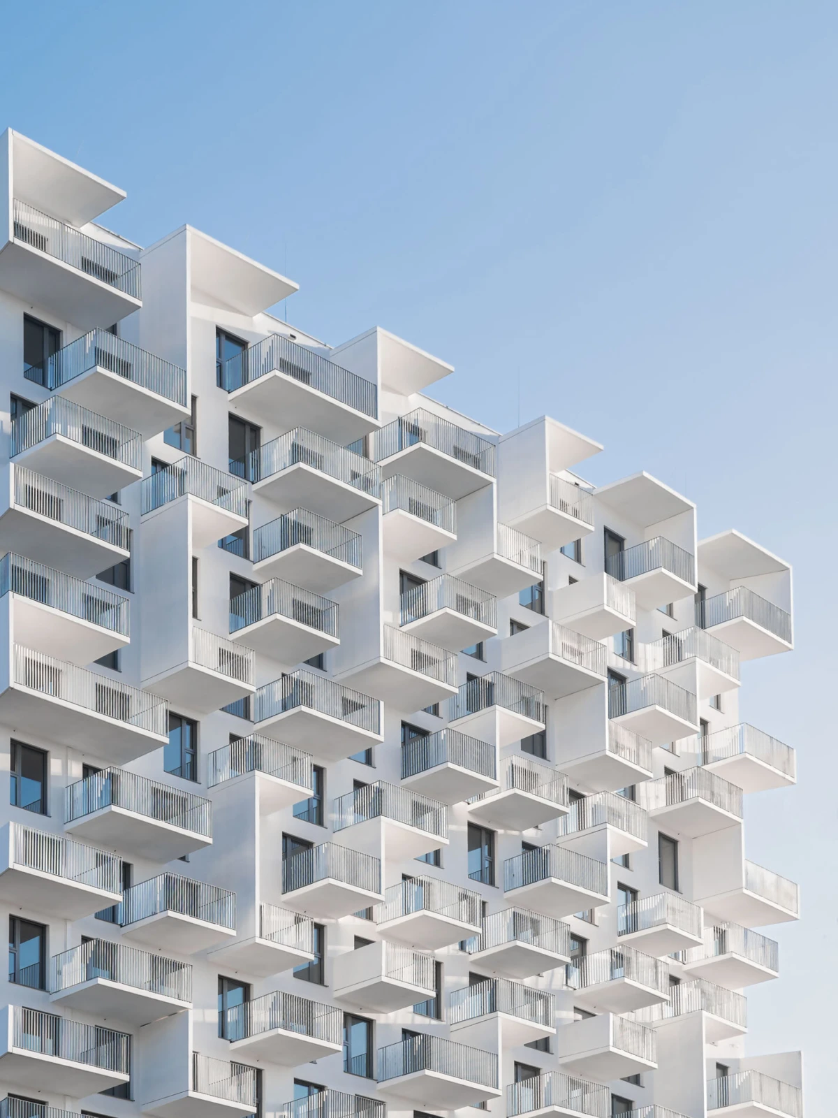 White apartment building with stacked balconies against a clear blue sky.