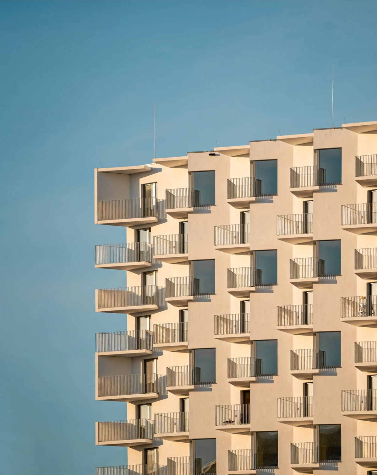 Beige modern apartment building with rows of balconies under a blue sky.
