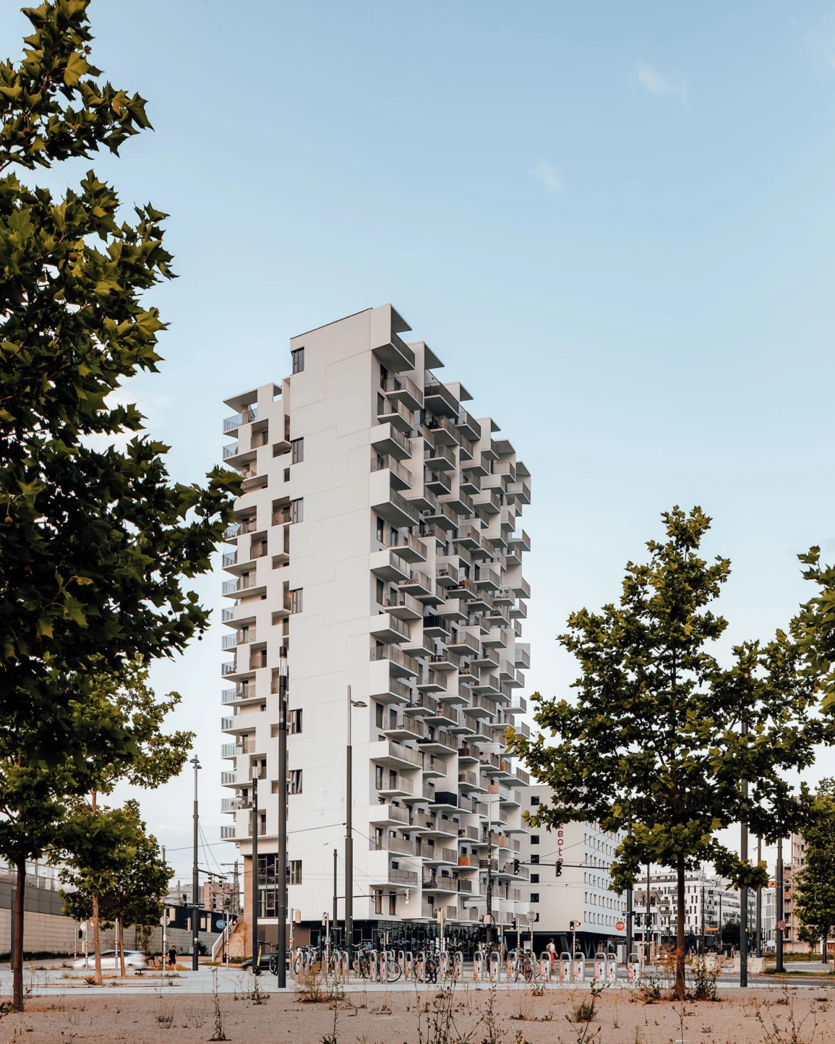 Tall white residential tower rises on a city street, framed by trees; bicycles parked at the base.