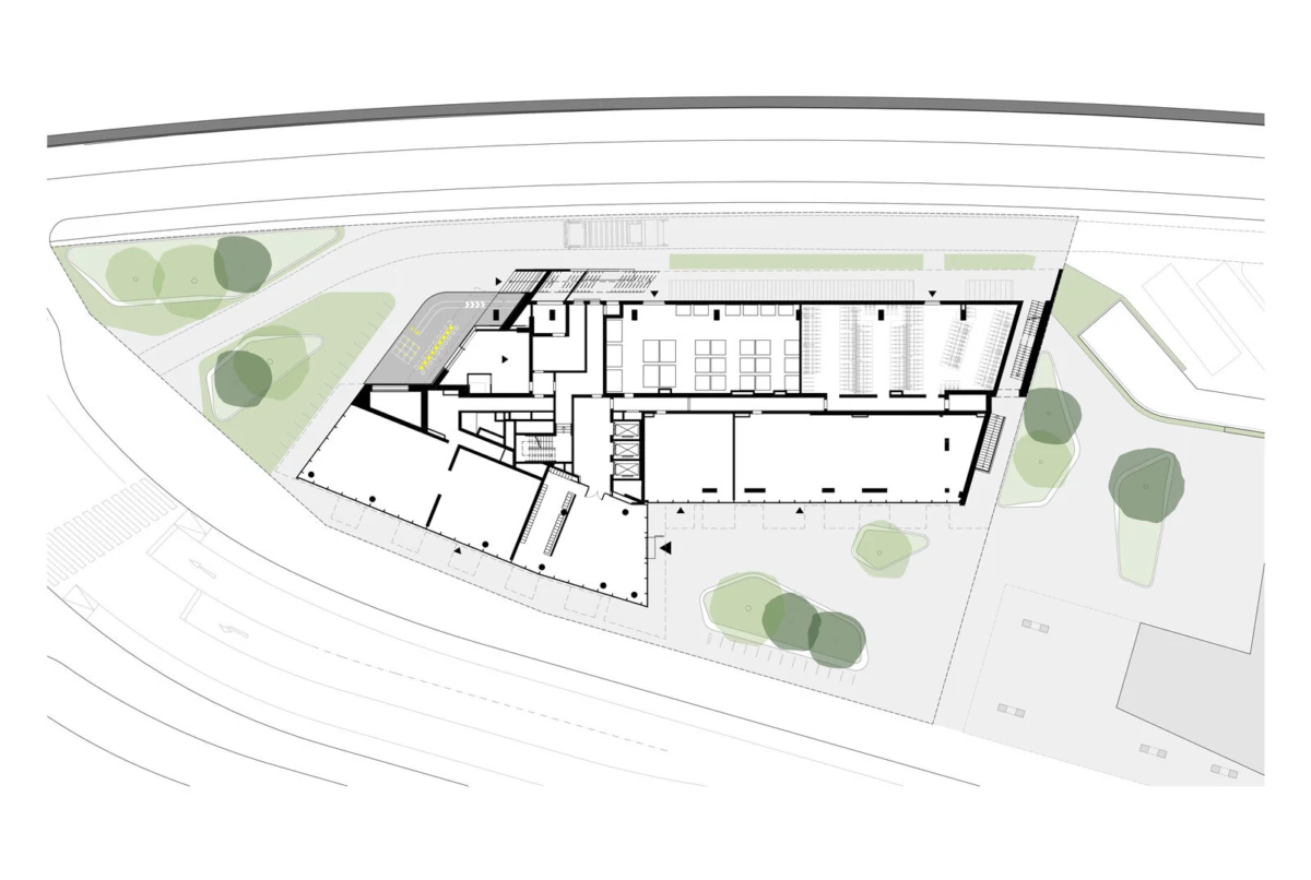 Architectural site plan of a building complex with surrounding landscaping, trees, and roads; railway tracks run along the top edge.