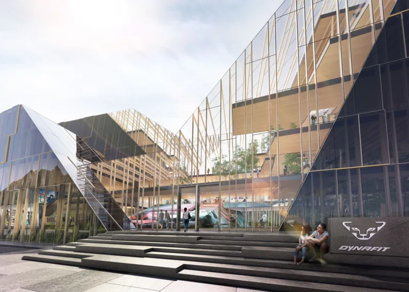 Glass-clad modern atrium with stepped exterior stairs; people walk and sit near the entrance; Dynafit logo on a stone block.