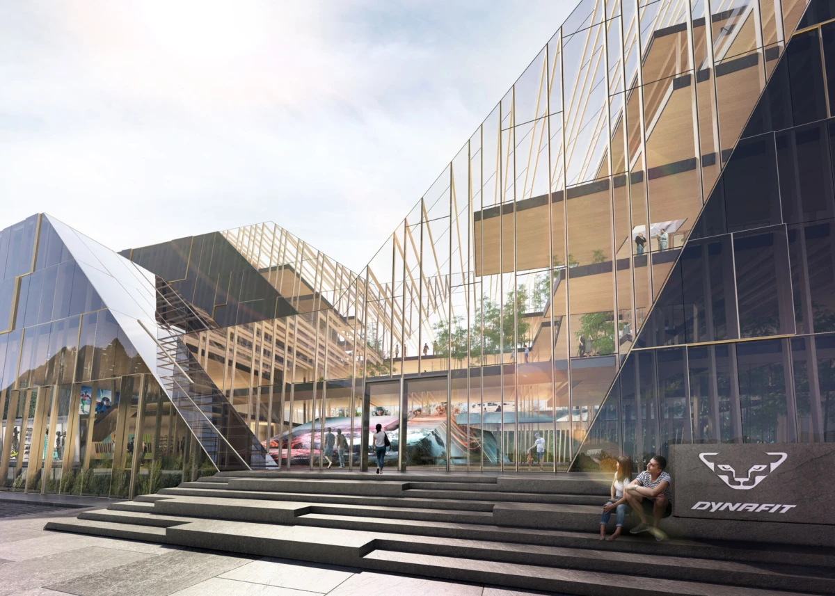 Glass-clad modern atrium with stepped exterior stairs; people walk and sit near the entrance; Dynafit logo on a stone block.