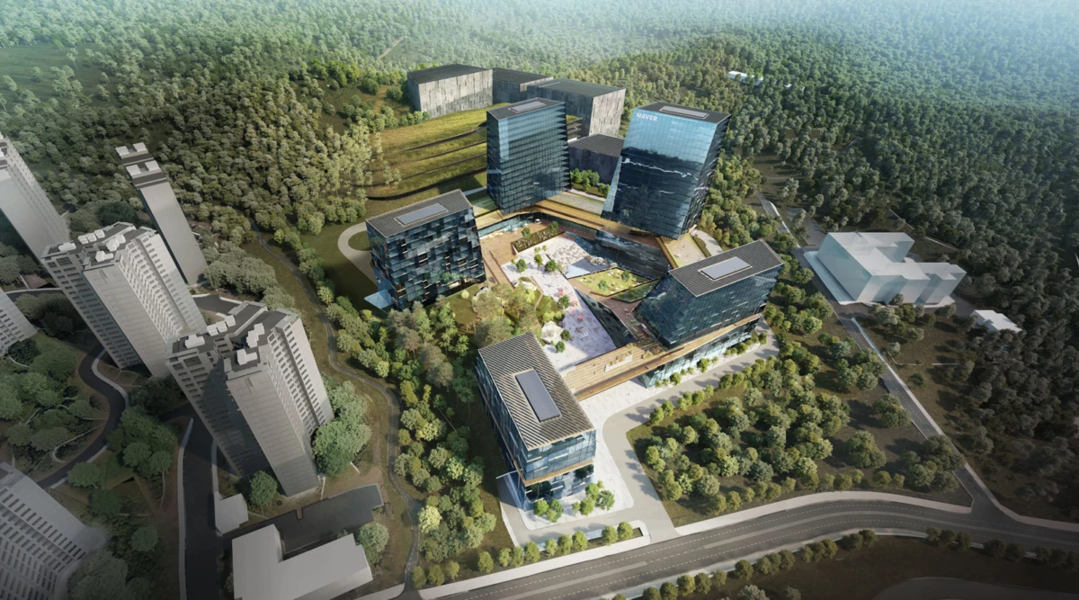 Aerial view of a glass-clad office campus nestled in dense woodland with interconnected buildings and green courtyards.