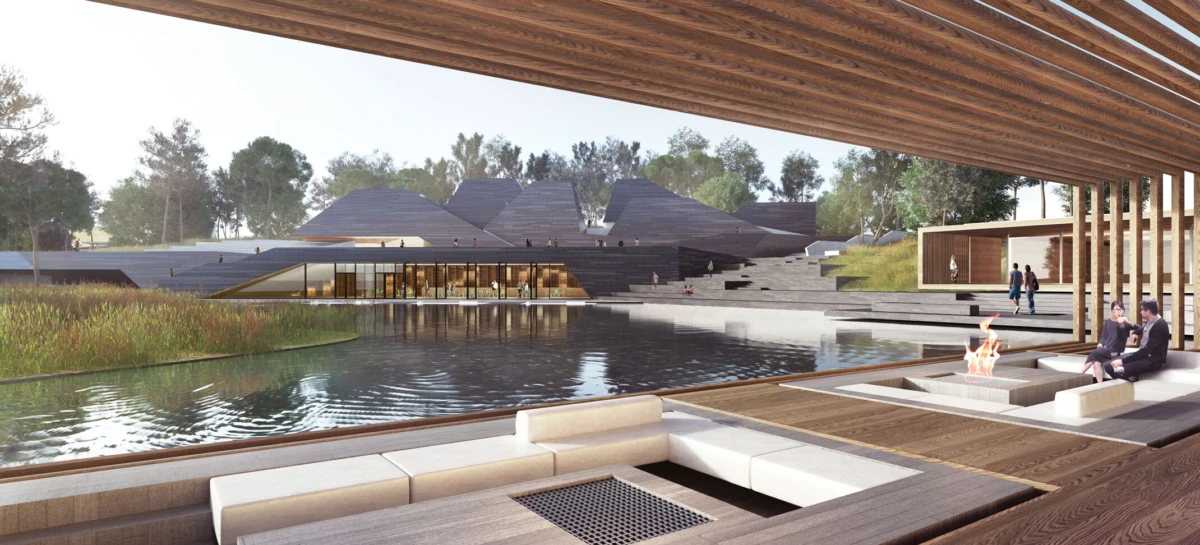 Modern architectural complex across a pond, with a wooden deck and fire-pit seating; people relax under a shaded pergola beside water.