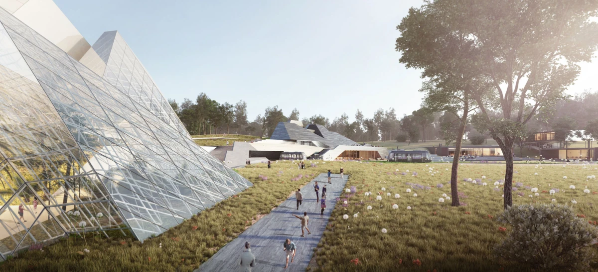 Glass pyramid building with triangular panes in a grassy plaza; people walk a central path toward low modern structures, trees, and open field.