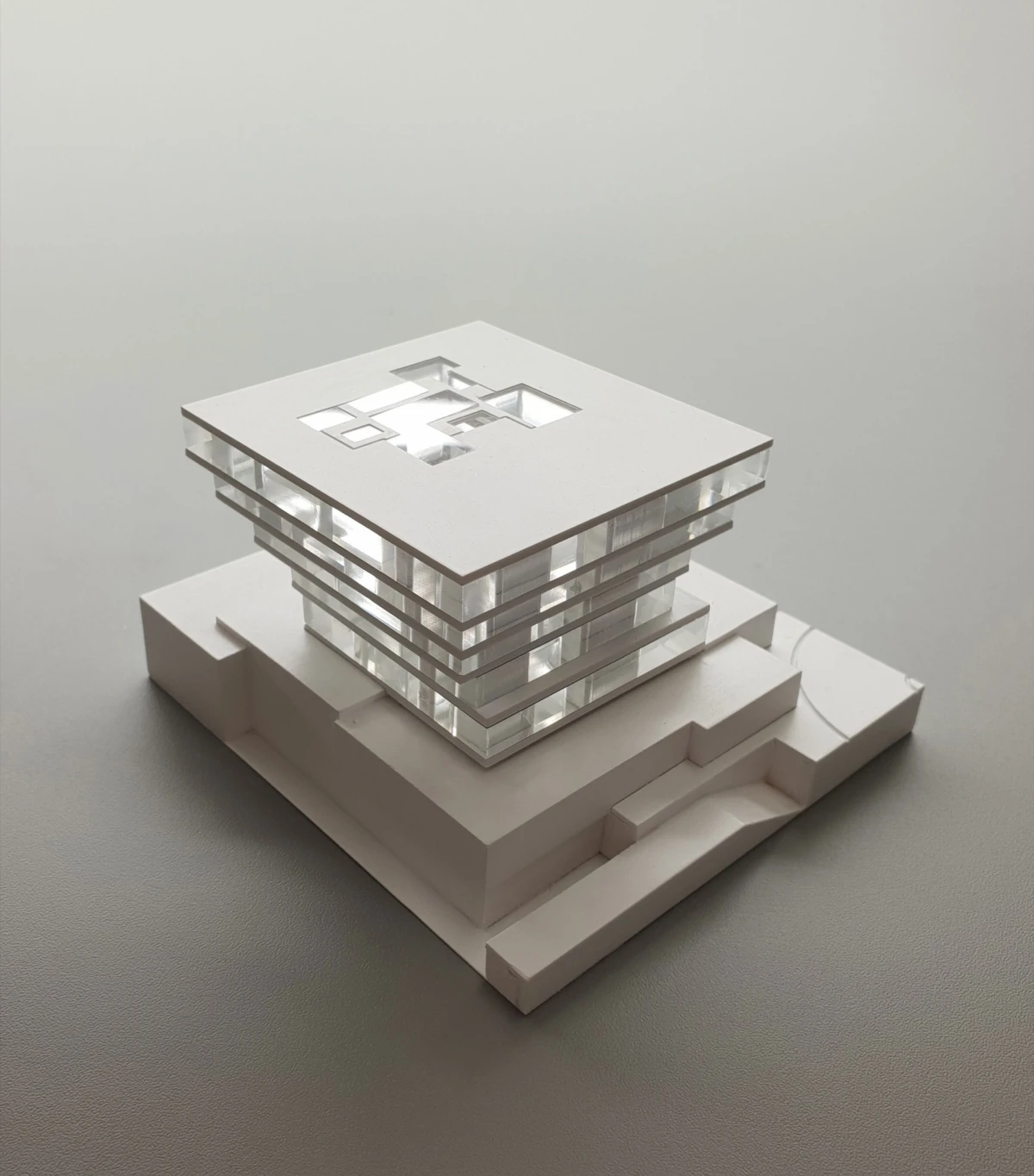 Architectural model of a modern glass building with stacked cubic floors and a square rooftop opening on a stepped white base.