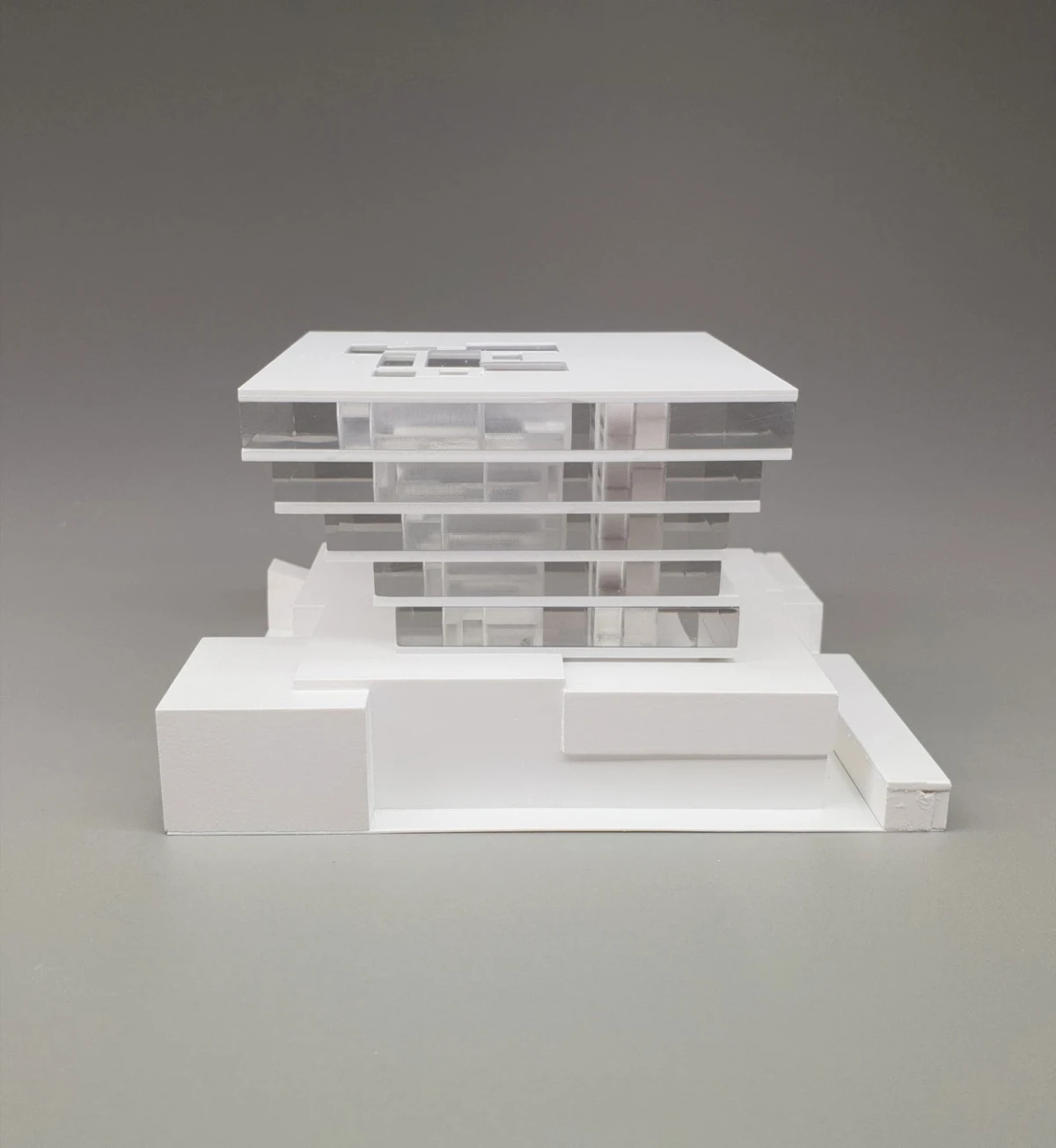 White architectural model of a multi-story glass office building with stacked, transparent floors on a stepped base.