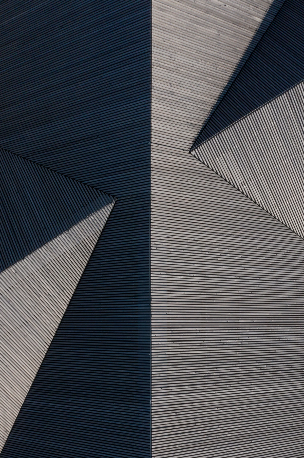 Close-up of an angular wooden-slat facade meeting at a sharp corner, featuring parallel grooves and dramatic shadows.