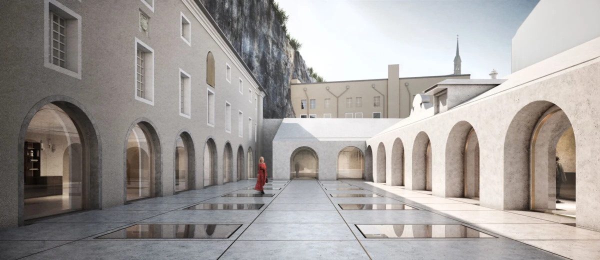 Person in a red garment walking across a stone courtyard bordered by arched colonnades with glass panels.