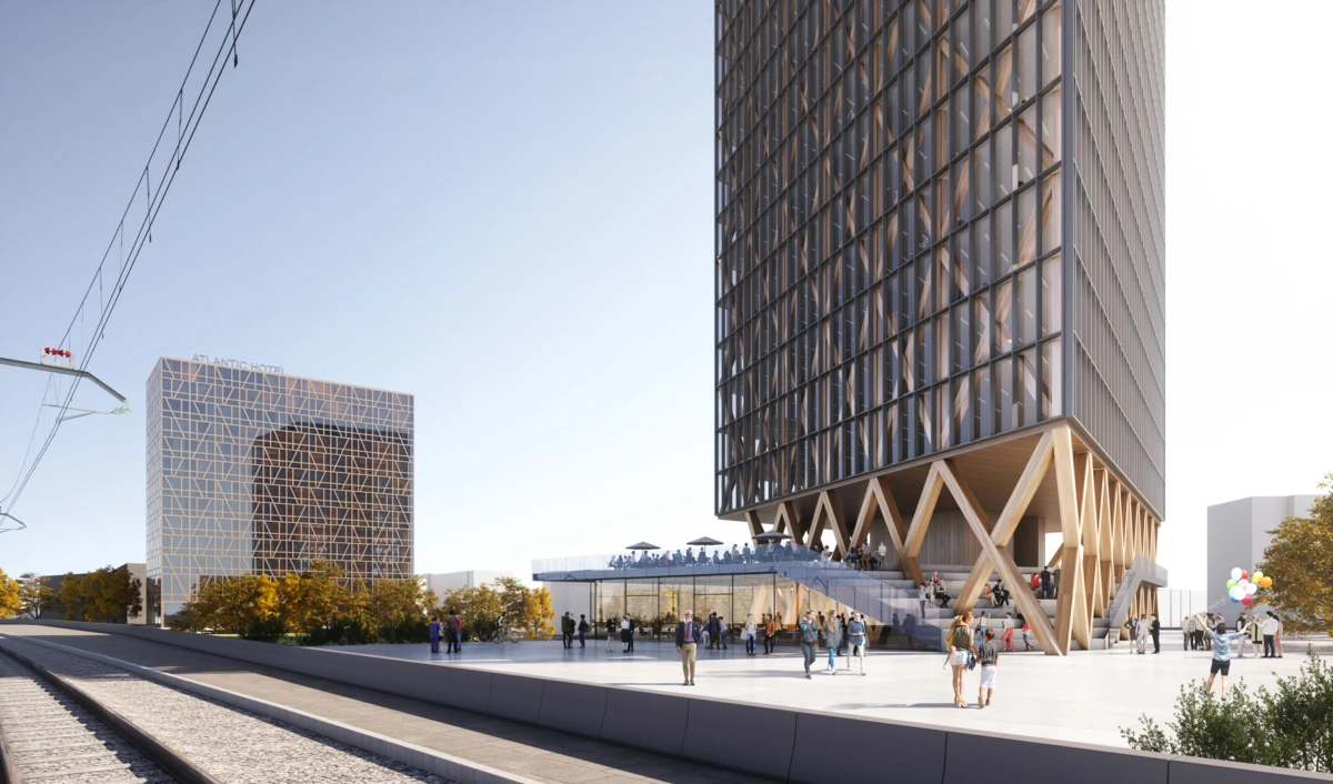 Tall glass-clad skyscraper with X-shaped wooden bracing at the base overlooks a busy plaza; rail tracks run along the left in a modern urban setting.