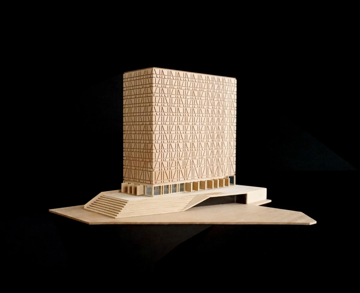 Wooden architectural model of a tall rectangular building with a crisscross lattice facade on a stepped platform with a ramp.