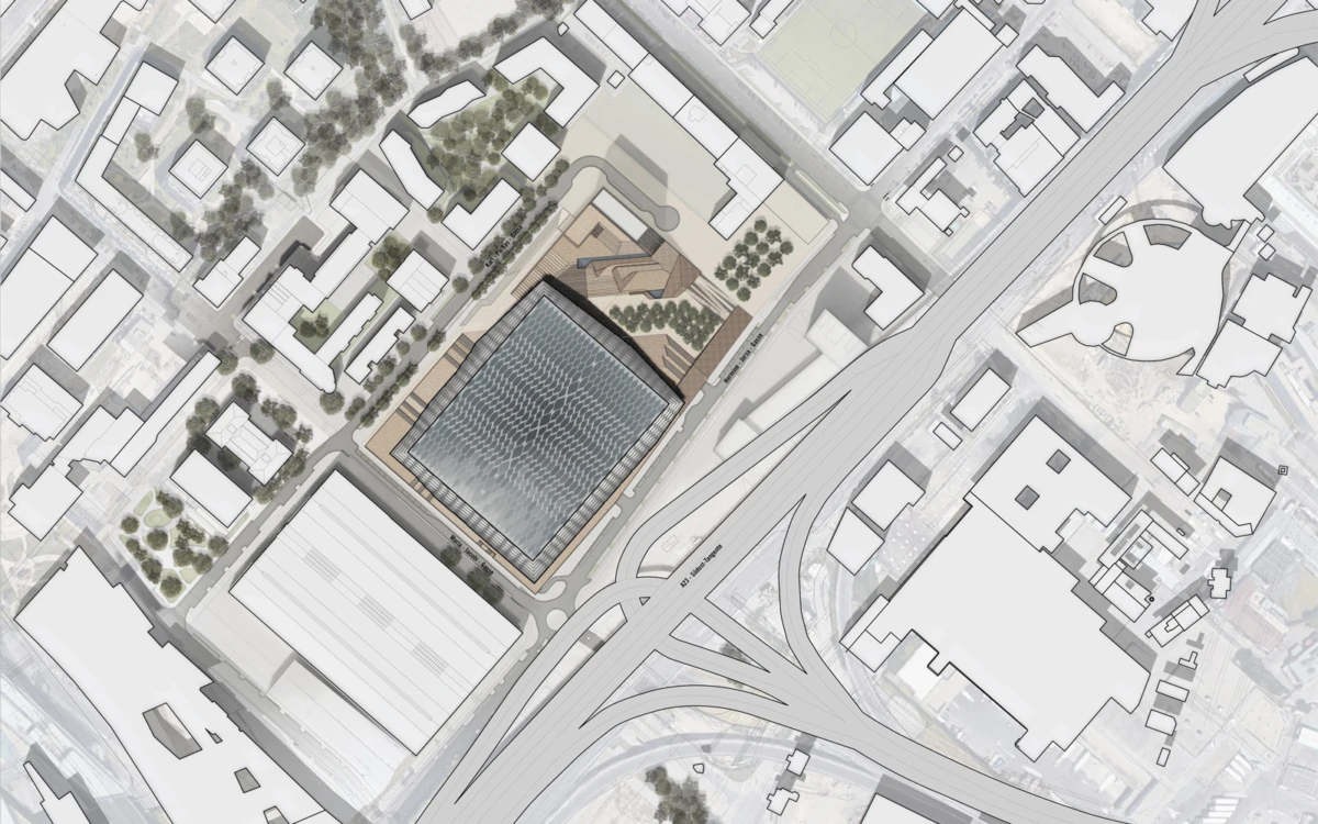 Aerial view of a city block with a glass-roofed square building at center, adjacent to a curved highway interchange and tree-lined streets.