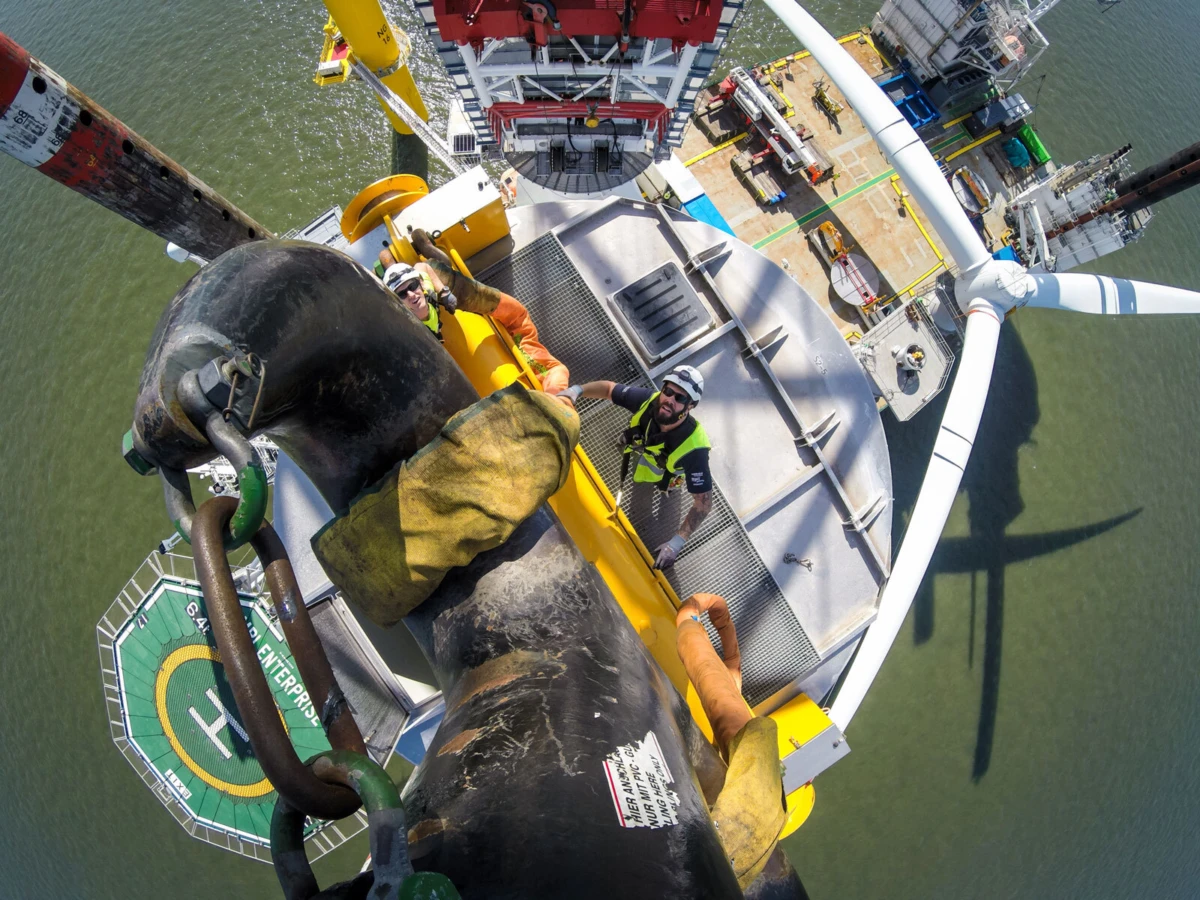 Two workers in safety gear atop an offshore wind turbine nacelle, performing maintenance with rotor blades nearby.